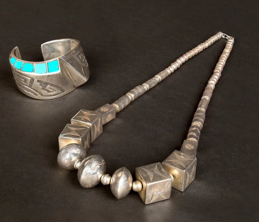 Handcrafted Navajo pearls necklace with large silver beads displayed beside a turquoise inlay silver cuff bracelet